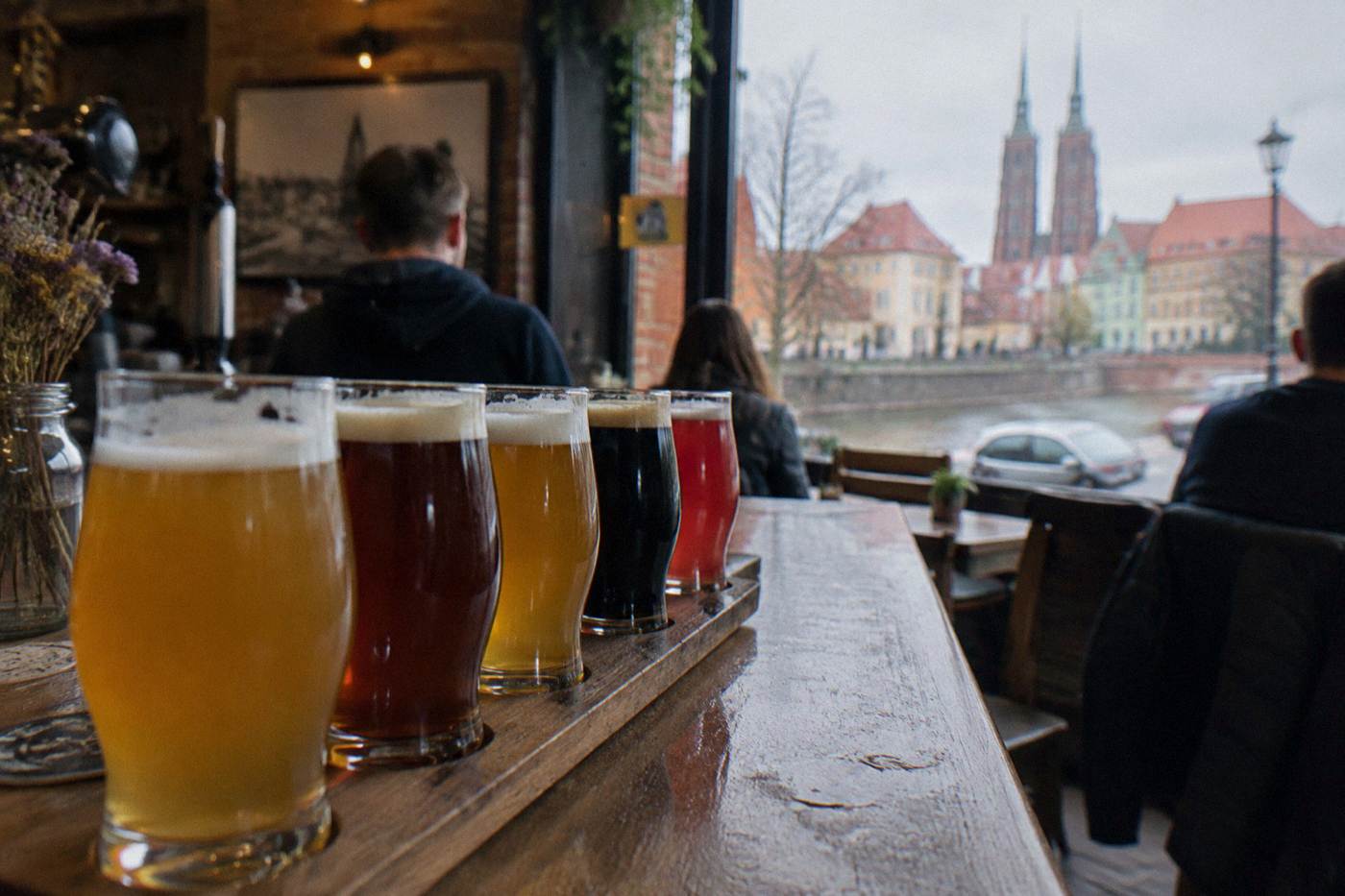 A row of craft beer glasses on a wooden bar counter in a cozy Wroclaw pub