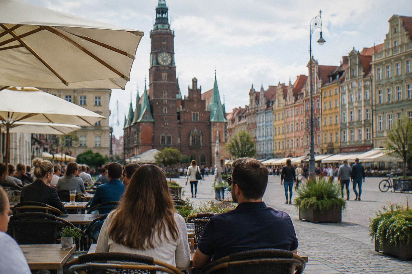 A market square cafe terrace in Wroclaw with customers at outdoor tables on a sunny afternoon