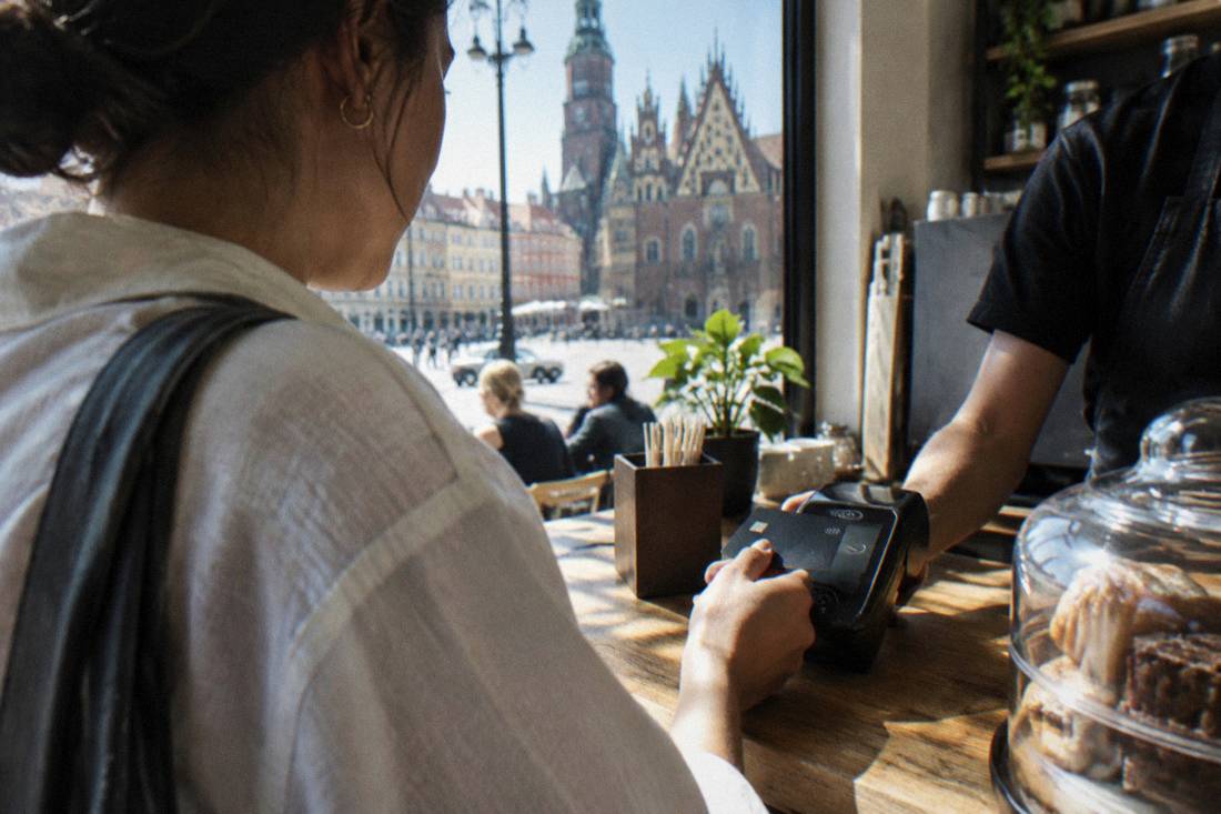 A customer tapping a contactless bank card on a payment terminal at a small cafe counter