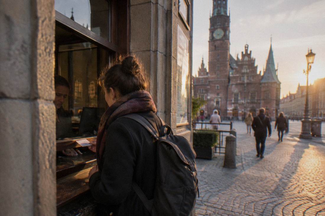A visitor buying a paper ticket at a museum counter window in Wroclaw