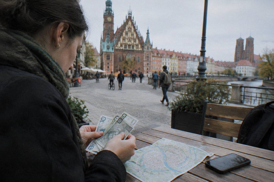 A traveler counting zloty banknotes at a wooden table beside a map and a phone