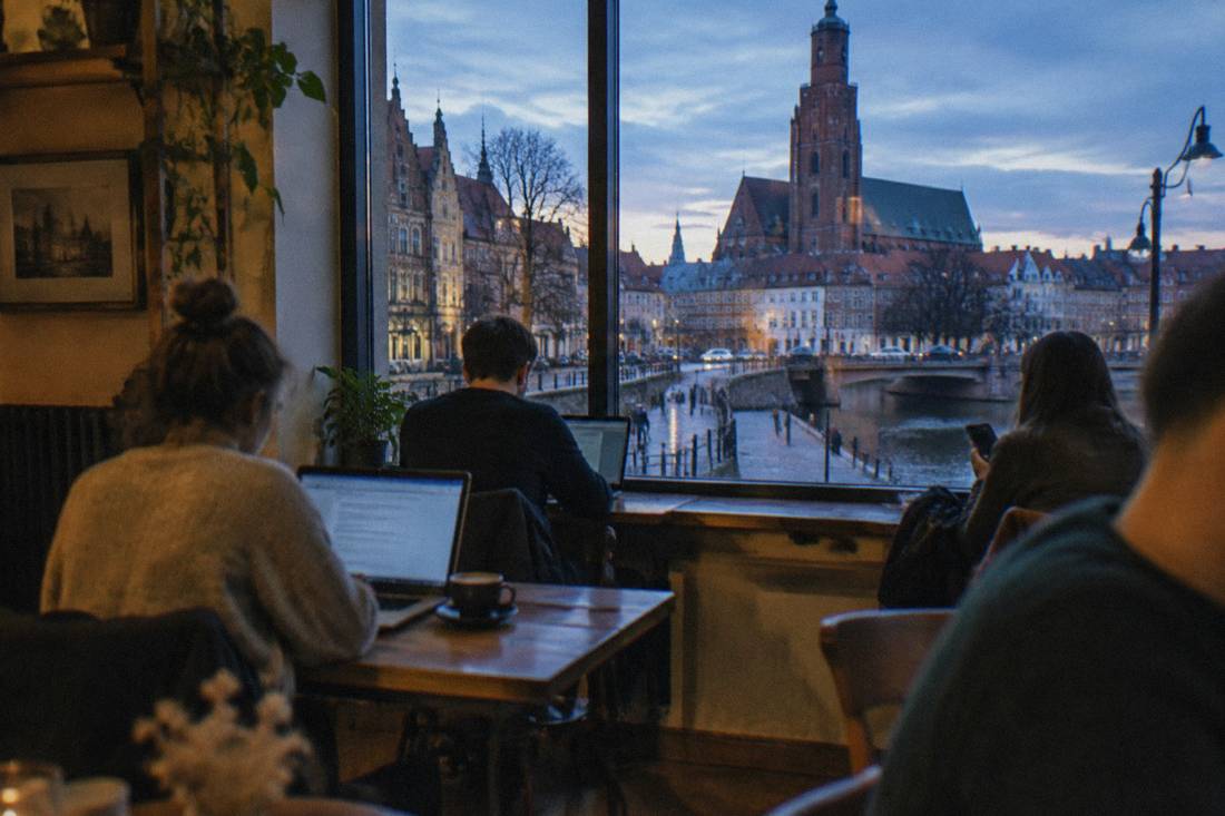 A cozy Wroclaw cafe interior with people using laptops and phones near a window
