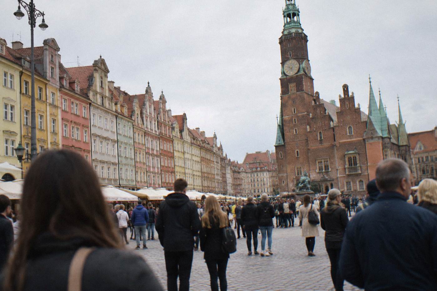 Crowds gathered on a large European market square in front of colorful painted townhouses