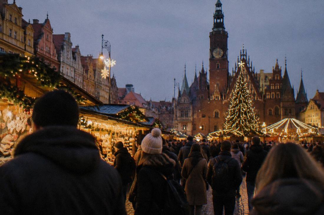 A lit Christmas market at night with wooden stalls, strings of lights and a crowd in coats