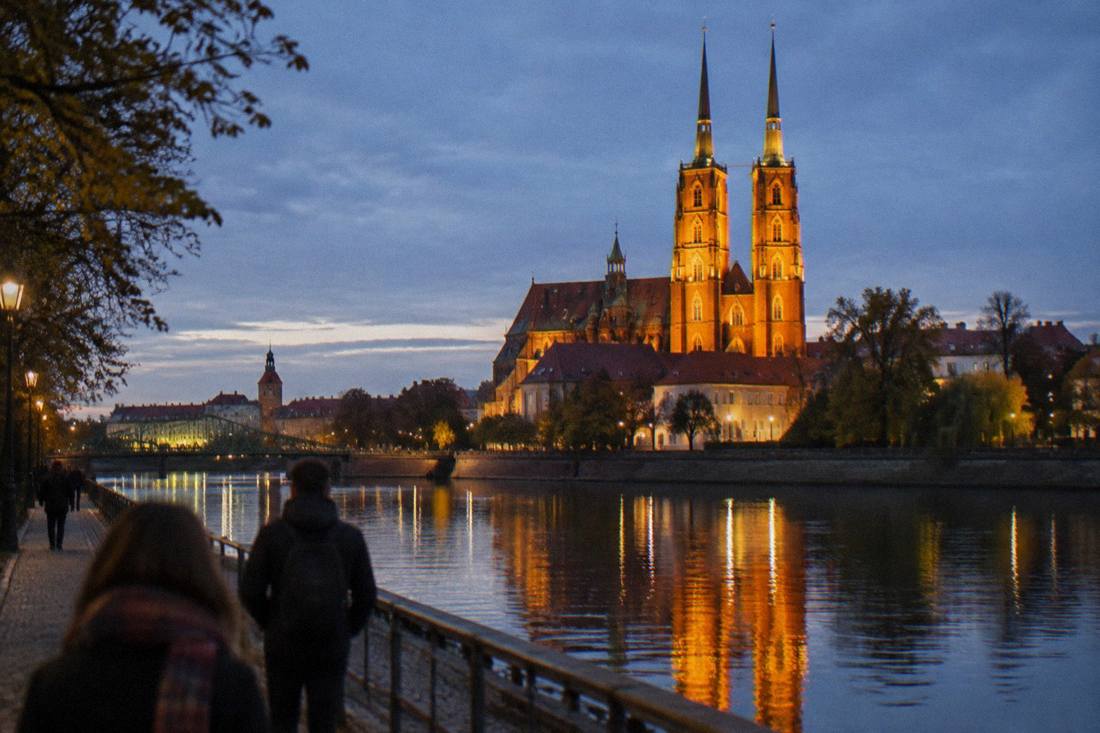 An evening view of a floodlit cathedral on a river island with reflections on the water