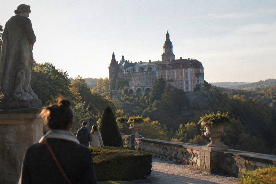 A large castle on a hill above forested slopes seen from a garden terrace