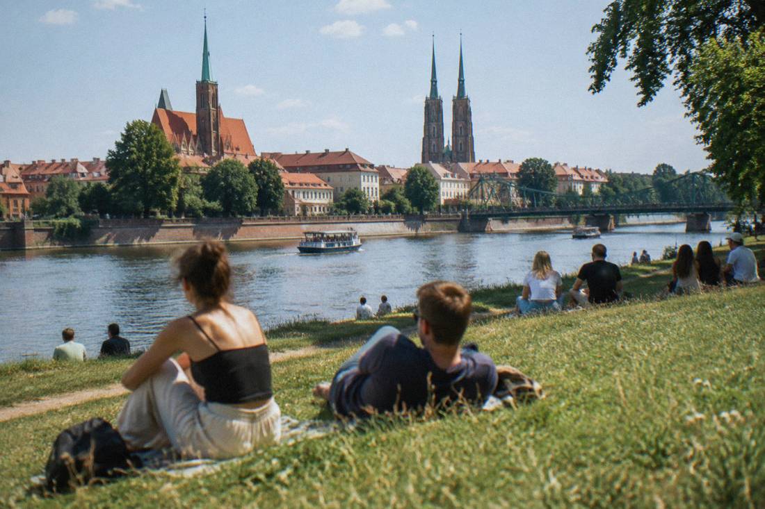 People relaxing on a grassy river island in Wroclaw beside the Odra on a warm summer afternoon
