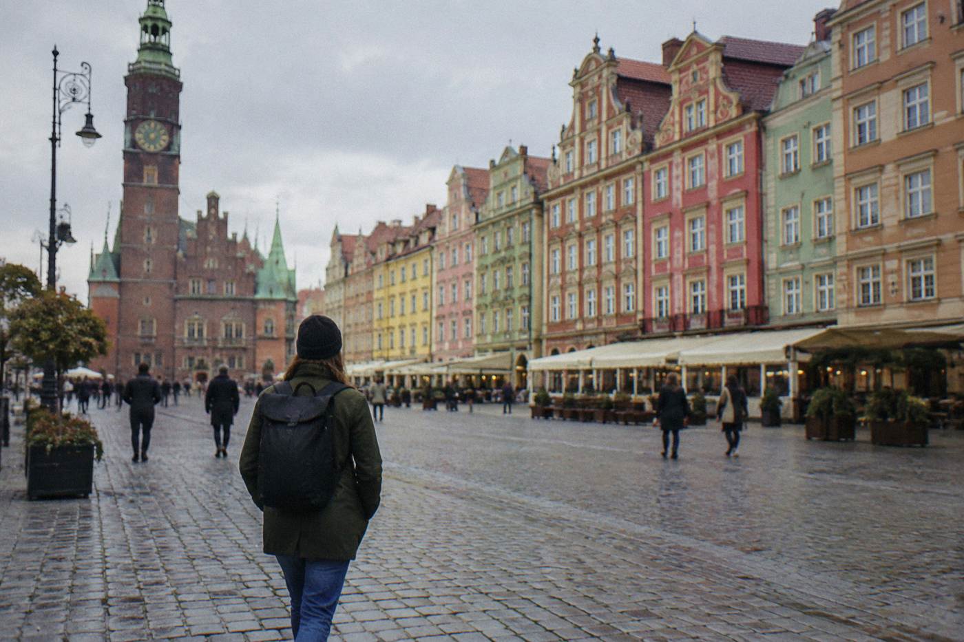 A traveler walking alone across Wroclaw Market Square past colorful townhouses
