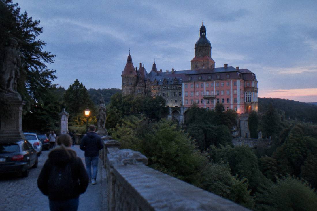 A large baroque castle on a hill surrounded by forested parkland in Lower Silesia