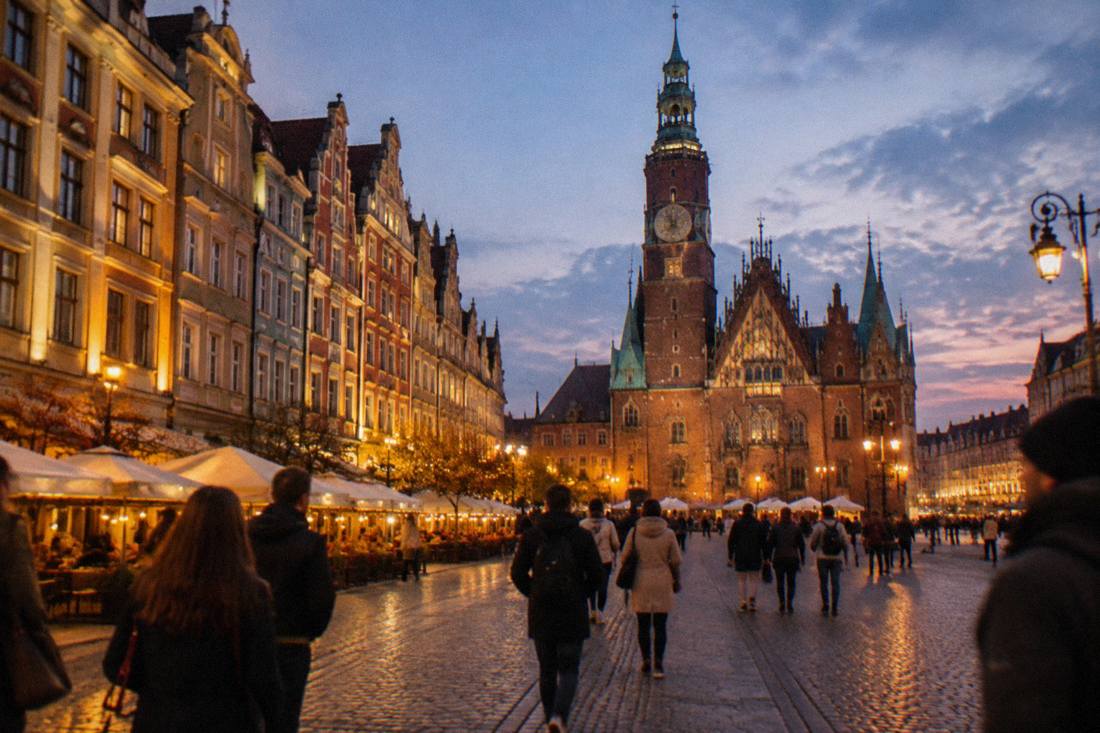 Wroclaw's market square at dusk with illuminated townhouses, the gothic town hall and people walking