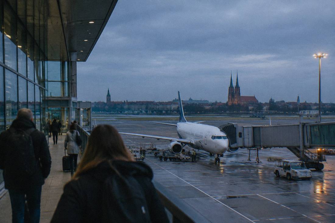 A modern airport terminal exterior with a plane at the gate under a gray sky