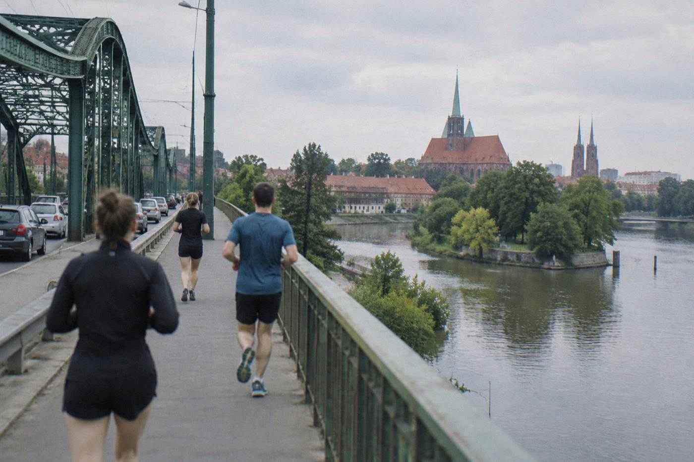 Runners crossing a bridge over the Odra river in central Wroclaw on a bright morning.