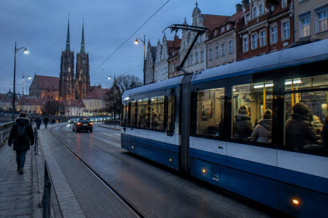 A modern tram moving along a street in central Wroclaw with passengers on board.