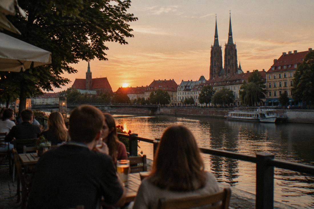 People drinking at outdoor tables beside a river at dusk