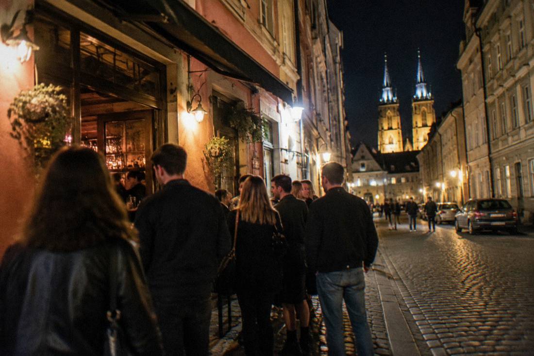 A small crowd outside a bar in a narrow old town street at night