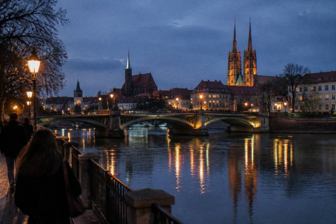 A stone bridge over a river with lit lamps reflected in the water at night