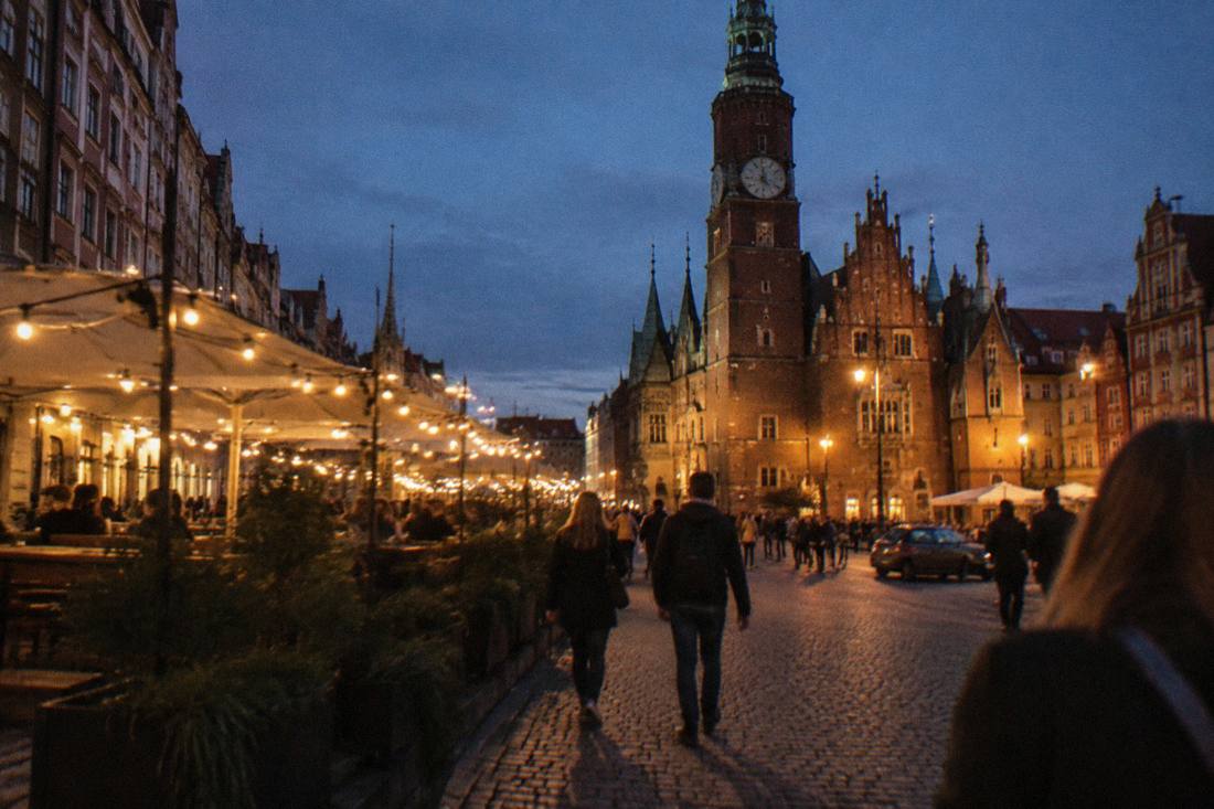 A historic square at night with strings of lights above outdoor seating