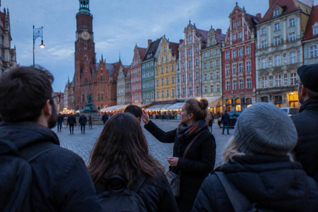 A walking tour group listening to a guide beside the colorful townhouses of the Wroclaw Market Square