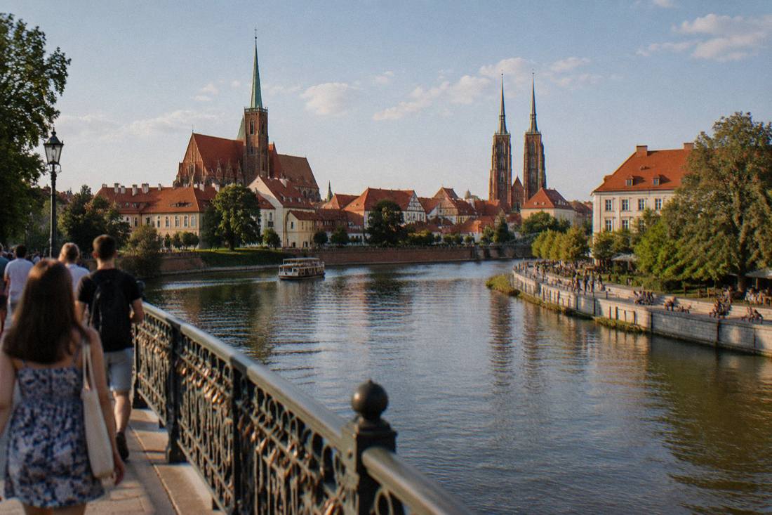The Odra river and Wroclaw old town seen from a bridge in summer with people walking along the bank
