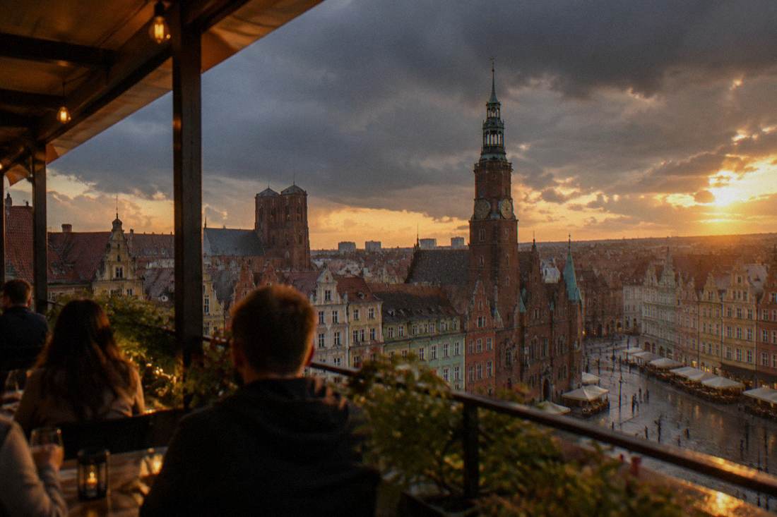 Rain clouds passing over Wroclaw rooftops and the Market Square towers, viewed from a covered rooftop terrace.
