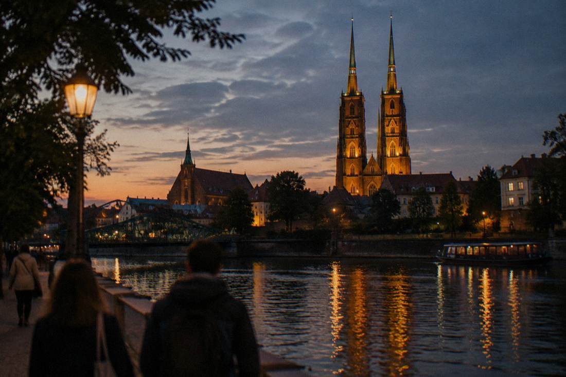 An illuminated gothic cathedral twin spires seen across a dark river at night