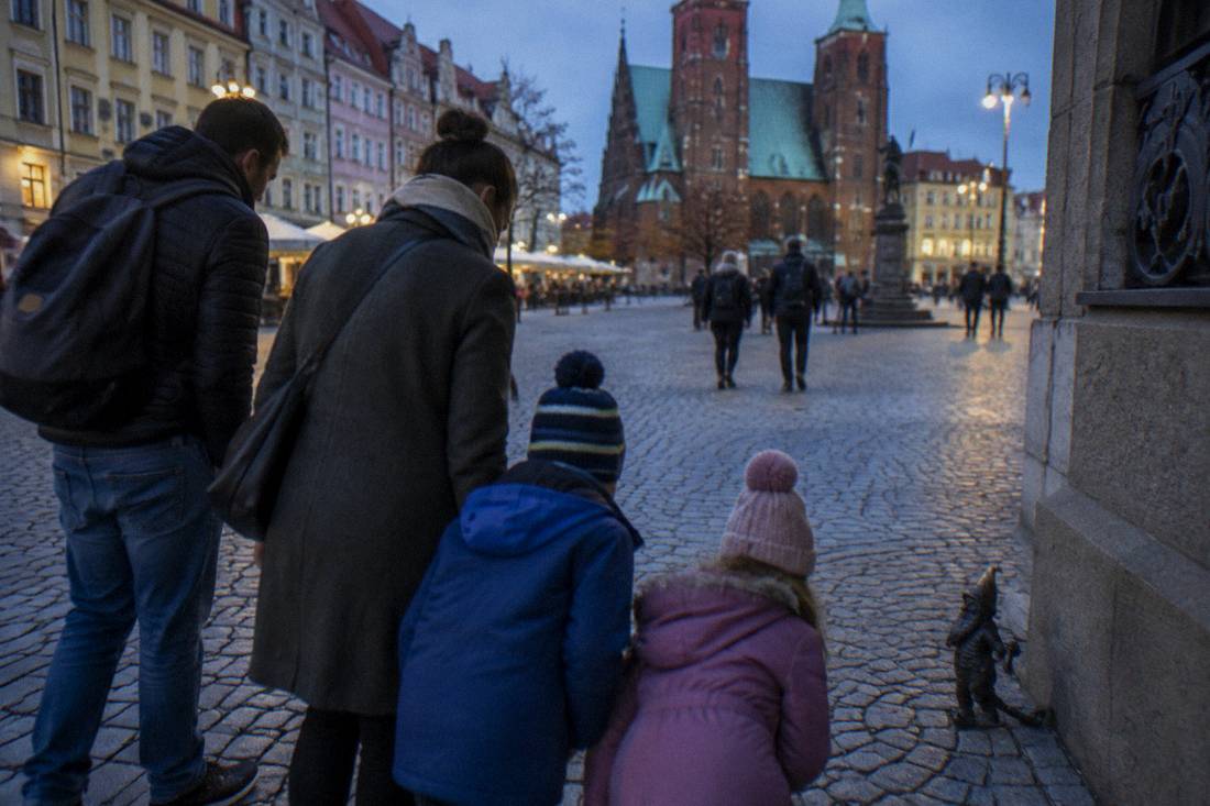 A family with children searching for a small bronze dwarf statue on a cobblestone square