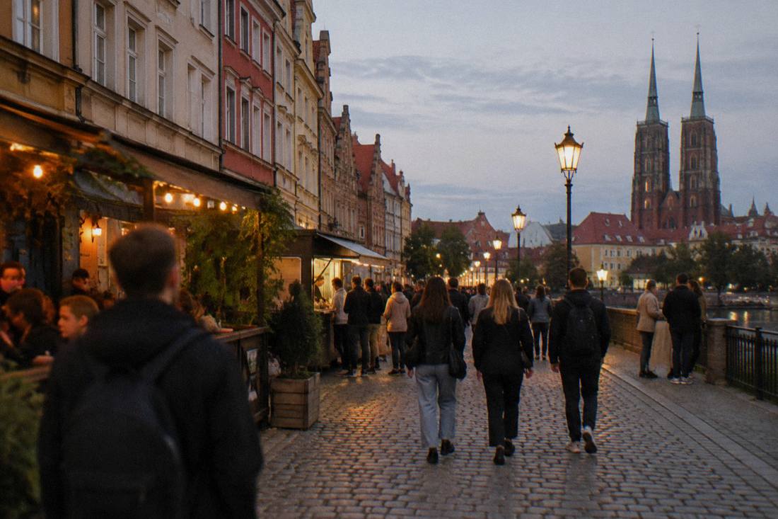An evening view of a lantern-lit street in Wroclaw with people walking between bars and food windows