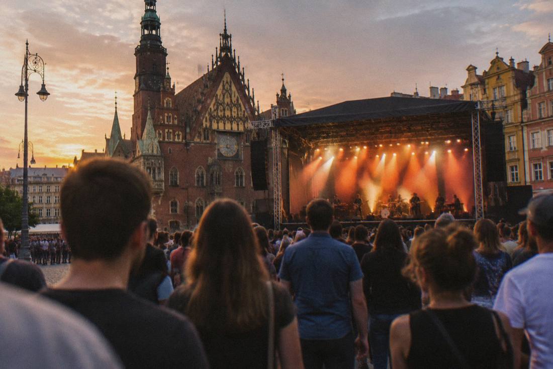 An outdoor concert crowd in a Wroclaw square with a stage lit in the evening