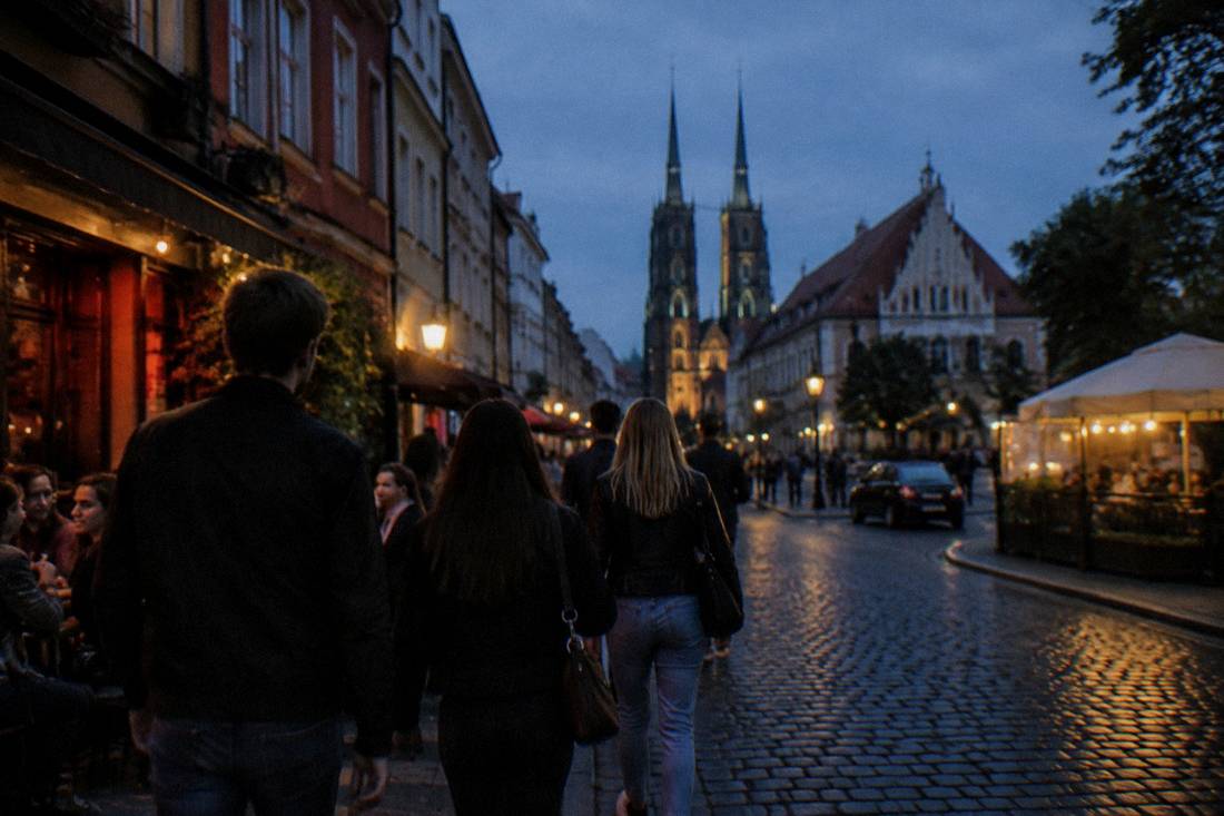 Friends in casual clothes walking between bars on a Wroclaw street at night