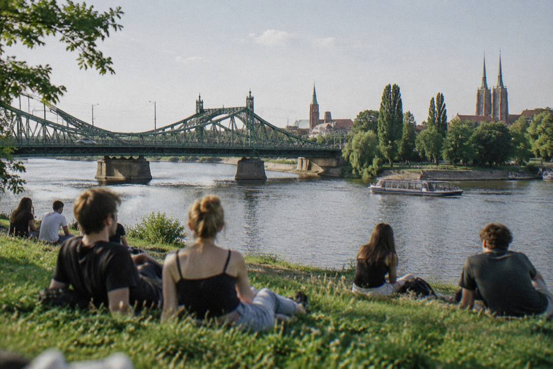 Young people sitting on grass by the Odra river on a sunny afternoon in Wroclaw