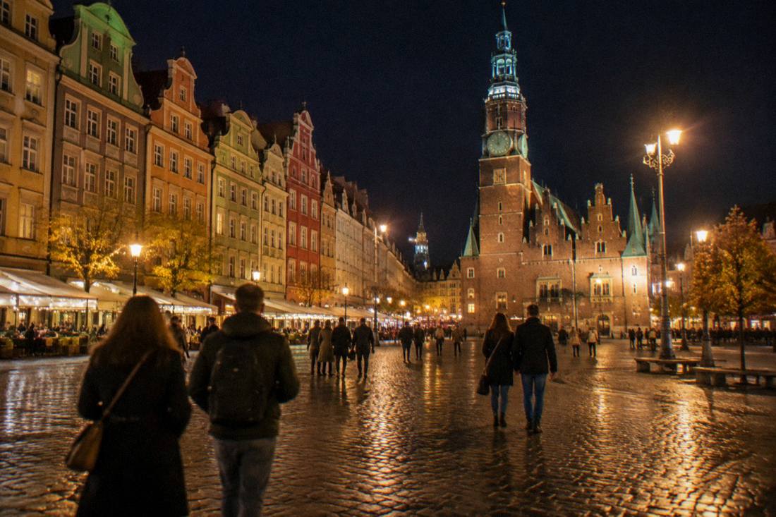 A wide view of the Wroclaw Market Square at night with lit facades and people walking
