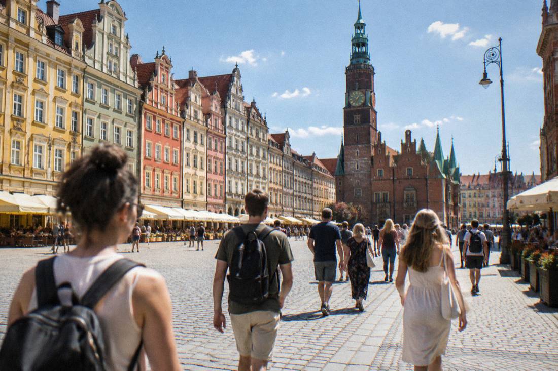 Tourists walking across a large historic market square lined with colorful townhouses