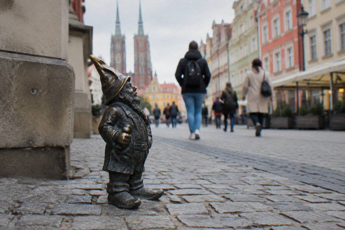 A small bronze dwarf statue standing on a cobblestone street in Wroclaw old town