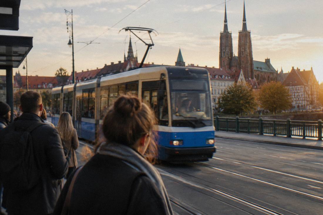 A tram moving along a street in central Wroclaw with passengers waiting at a stop
