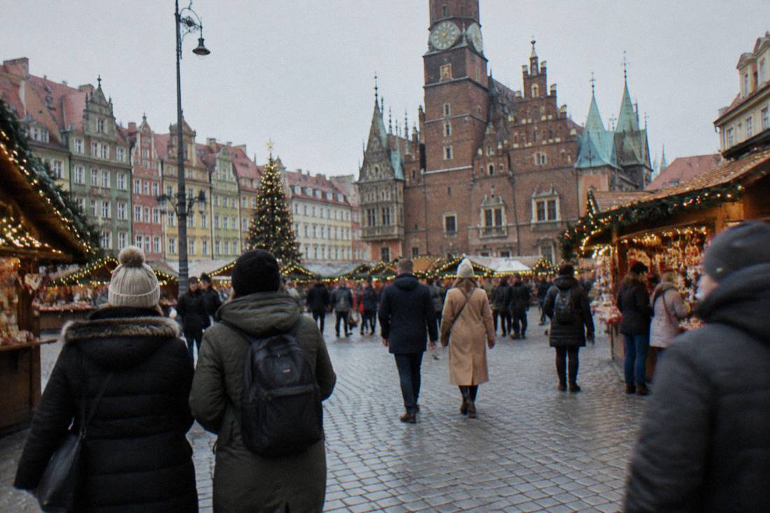 People in warm coats walking across Wroclaw Market Square with Christmas market stalls around the edges