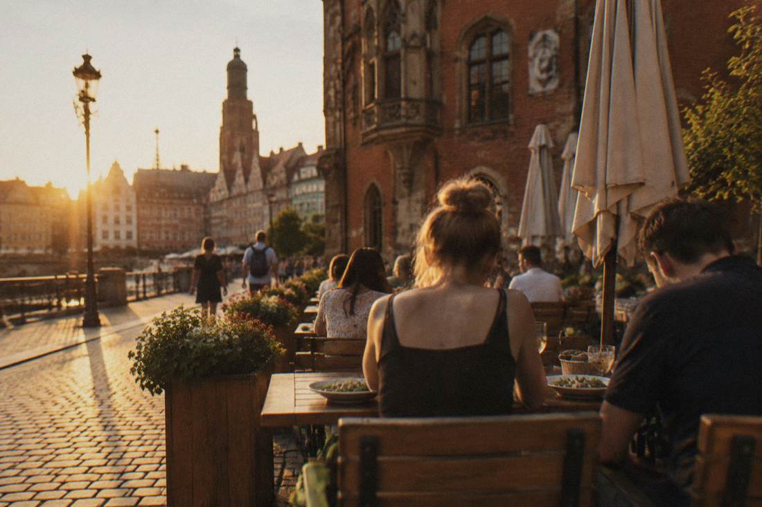 People eating at outdoor tables beside a historic building in warm weather