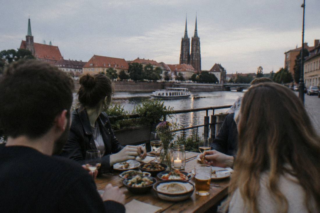 A group of friends sharing small plates at a wooden table in the evening