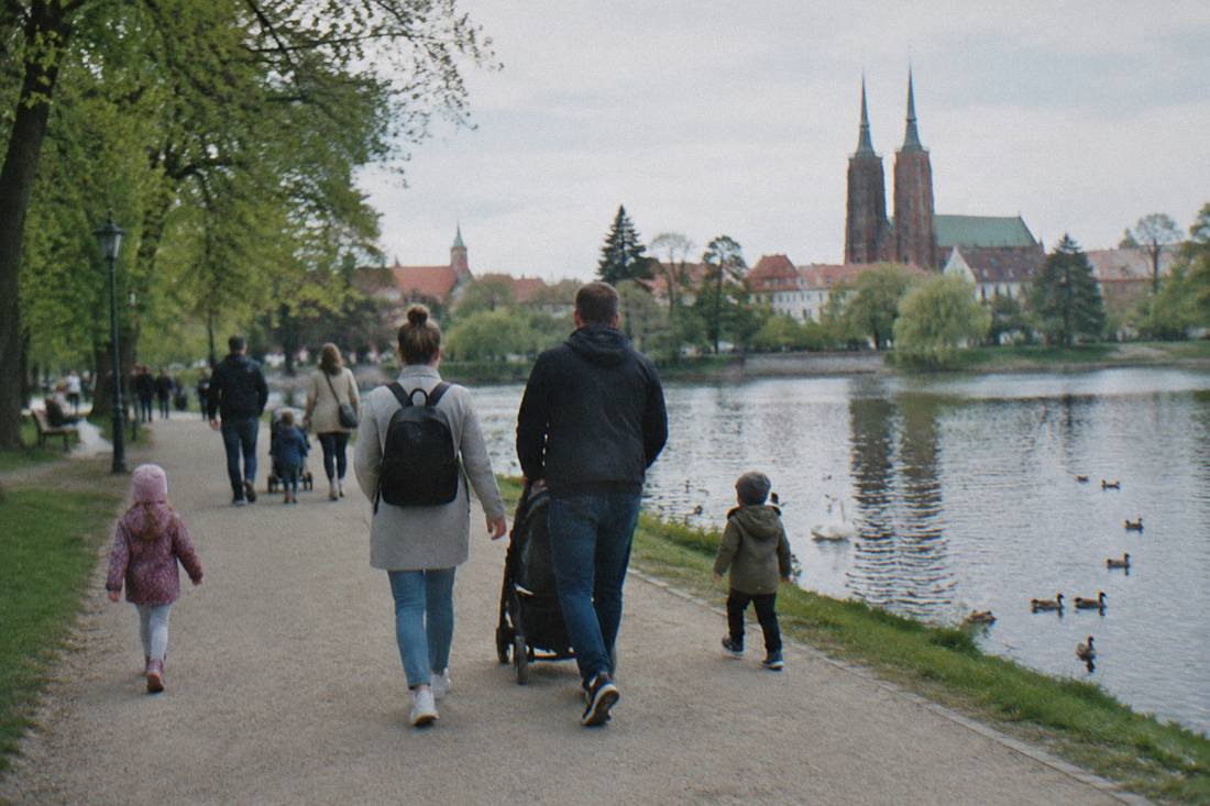 Families with children walking a wide path beside a pond in a park in Wroclaw