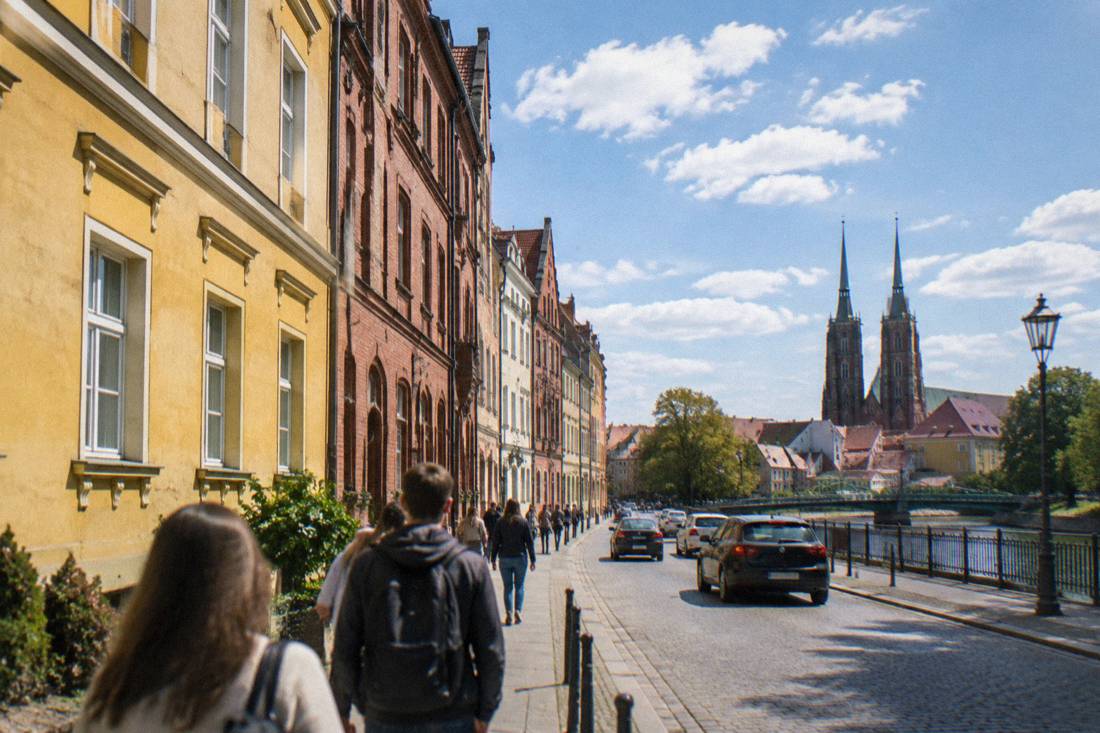Yellow and red brick townhouses on a Wroclaw street under scattered clouds