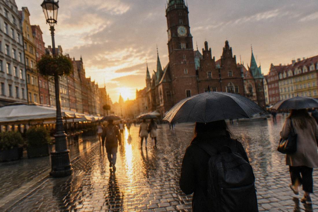 People walking with umbrellas across a wet cobblestone square in Wroclaw