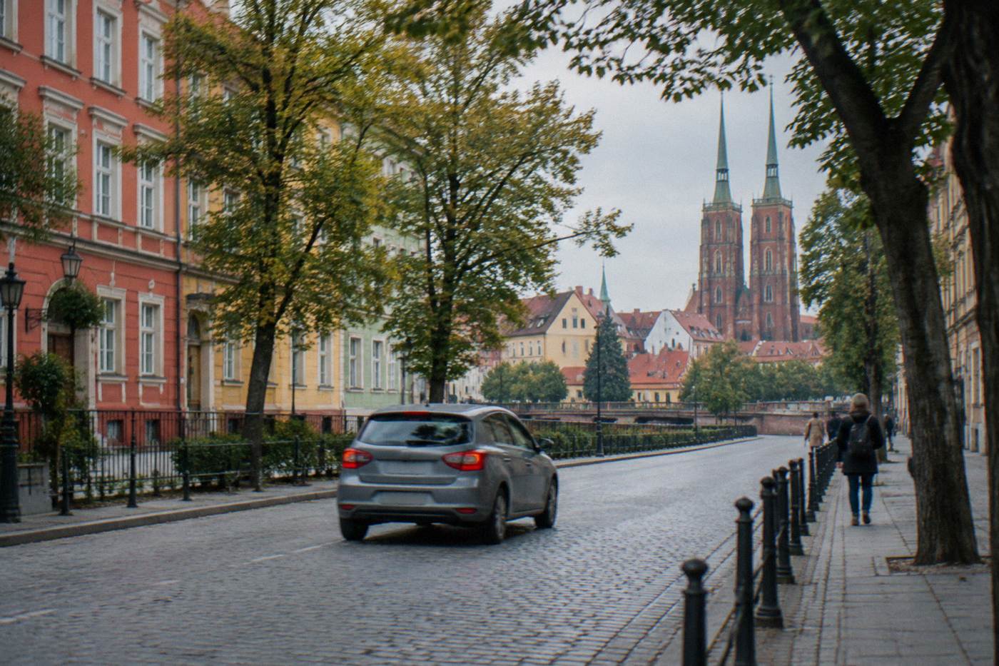 A car driving along a tree-lined street beside old colorful buildings in central Wroclaw