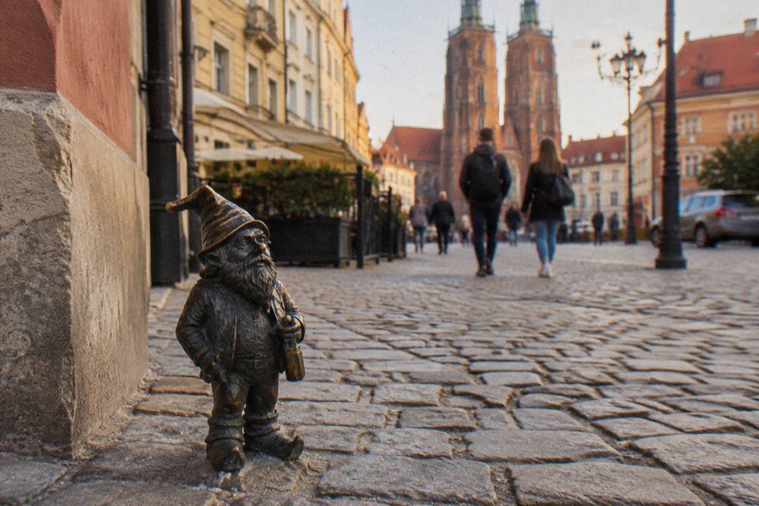 A small bronze dwarf statue standing on a cobblestone street in Wroclaw's Old Town