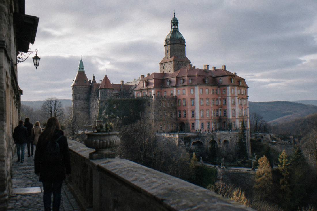 A large hilltop castle with towers and courtyards seen under a grey overcast sky