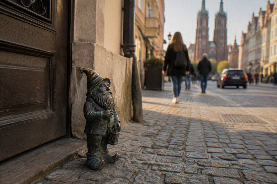 Small bronze dwarf statue standing on a cobblestone street beside a doorway in Wroclaw
