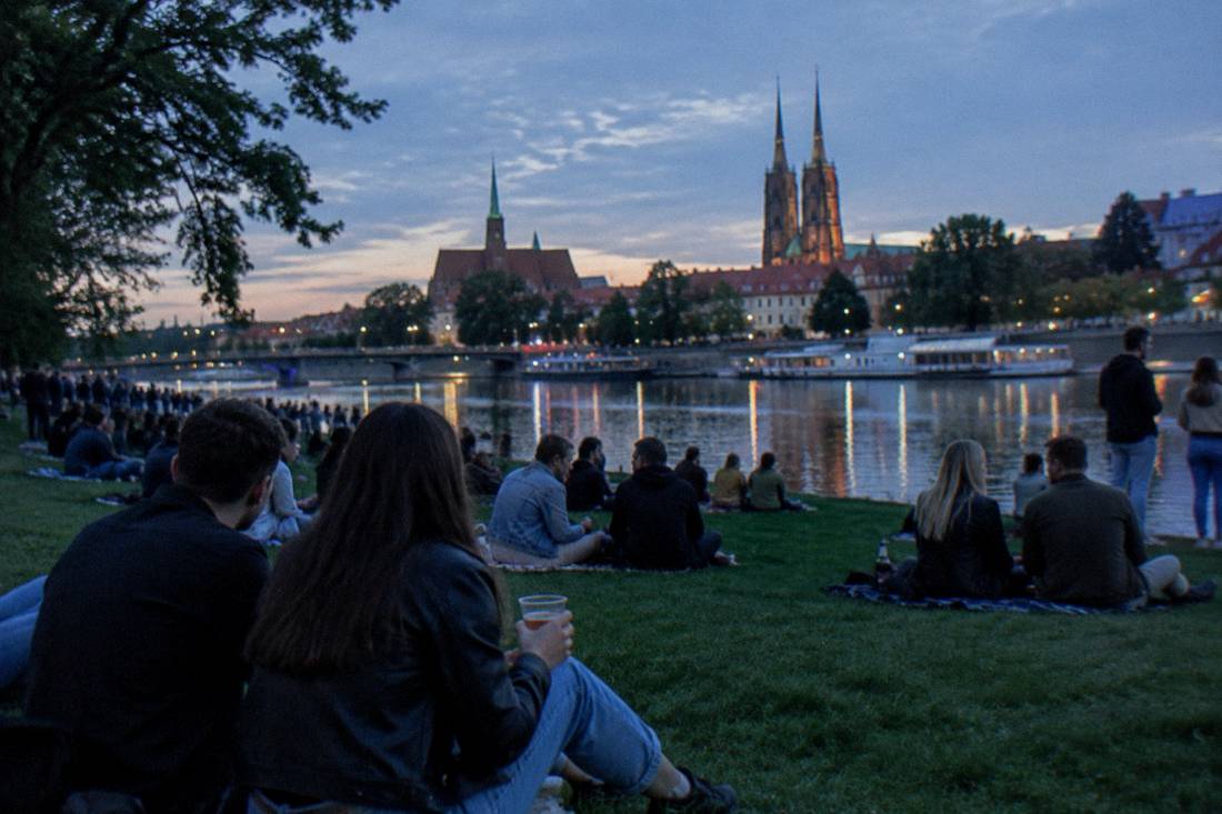Evening crowds with drinks on the riverbank lawns of Slodowa Island in Wroclaw