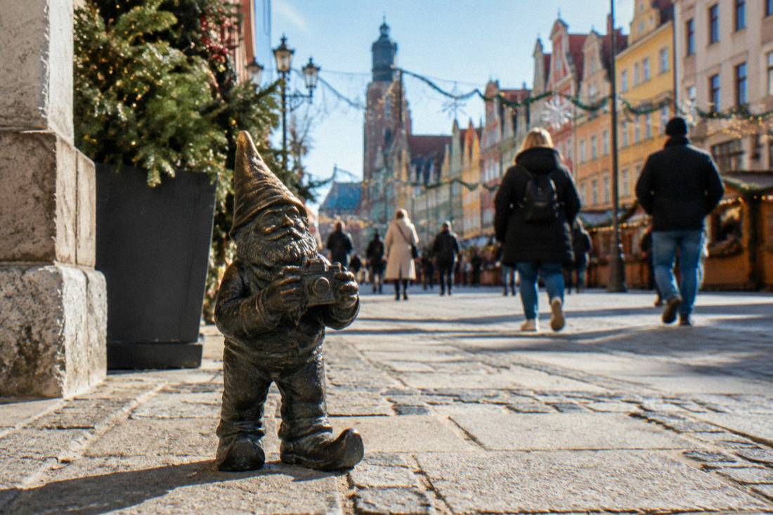 A small bronze dwarf statue on a Wroclaw street with festive lights in the background
