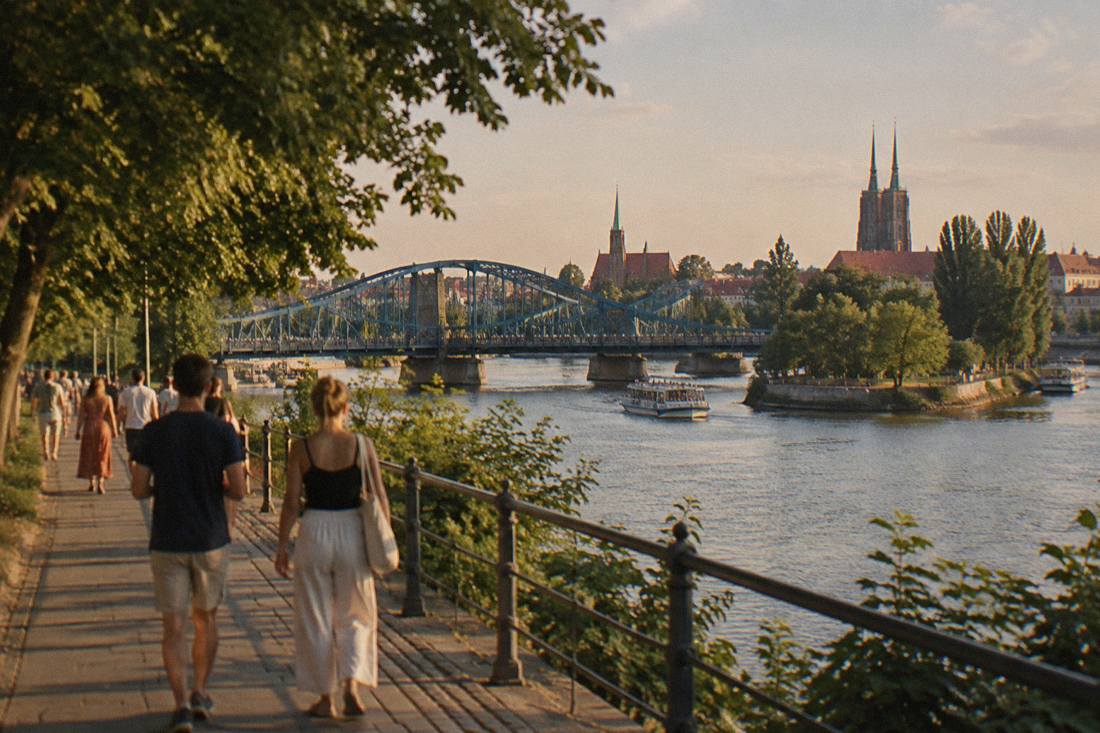 People strolling along a tree-lined Odra river promenade in Wroclaw on a warm afternoon