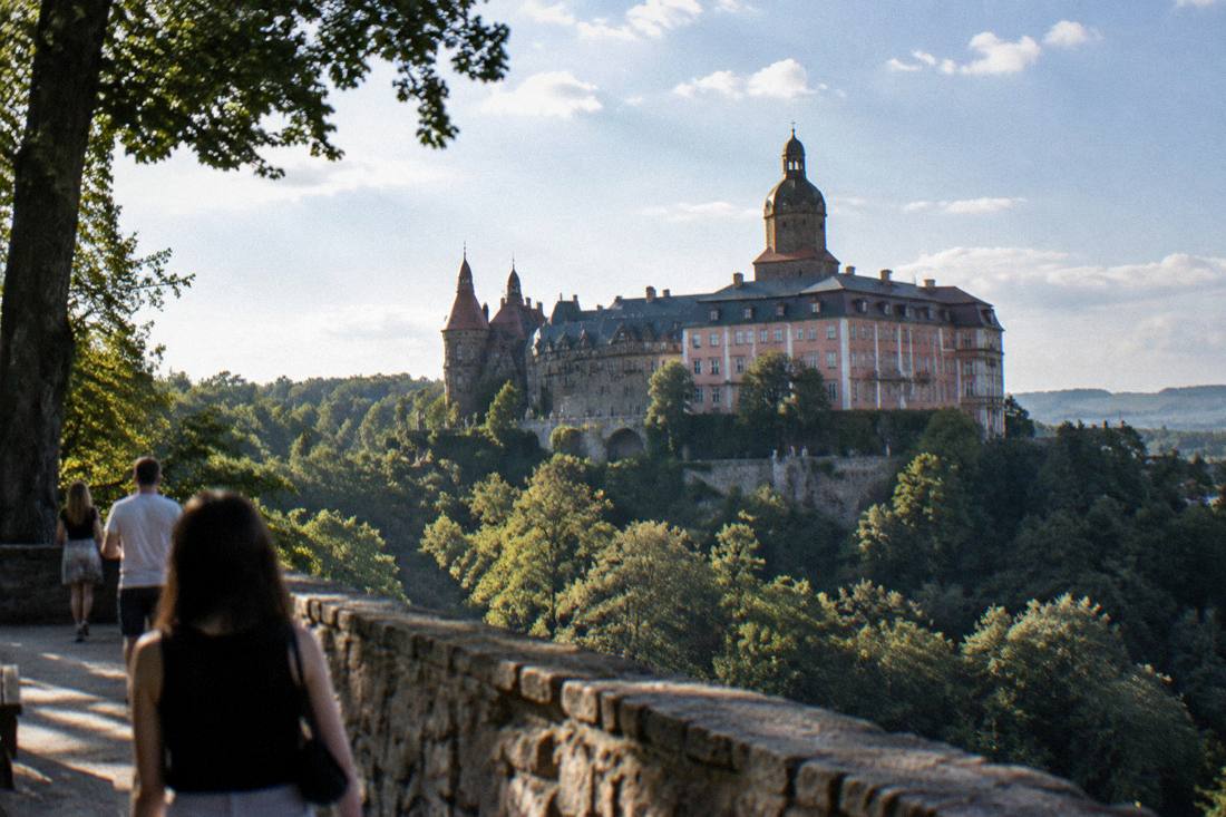 A view of Ksiaz Castle above its forested hillside under a summer sky
