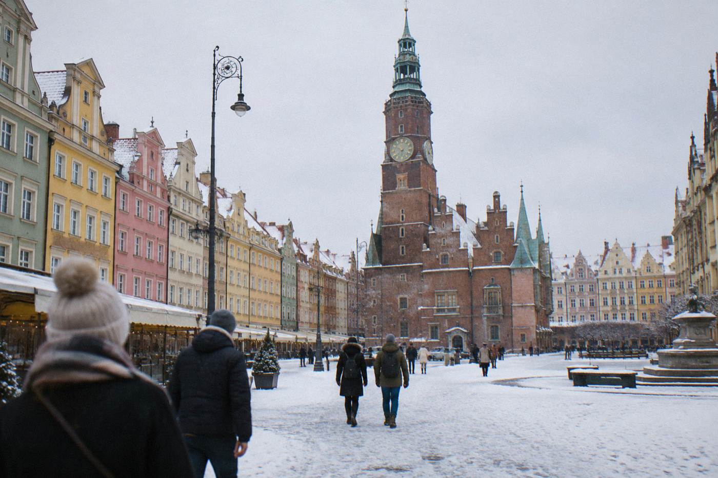 Wroclaw's market square dusted with snow, with pastel merchant houses and the Old Town Hall tower rising above the white square.