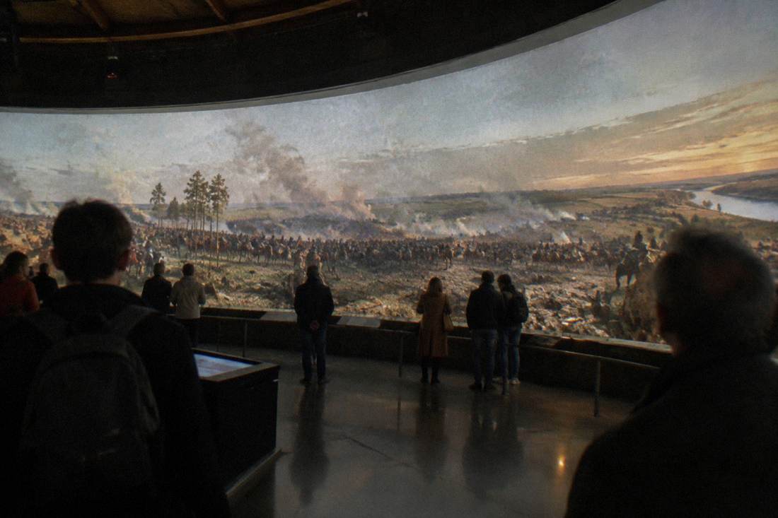 Visitors viewing a large panoramic painting inside a dimly lit circular rotunda gallery.